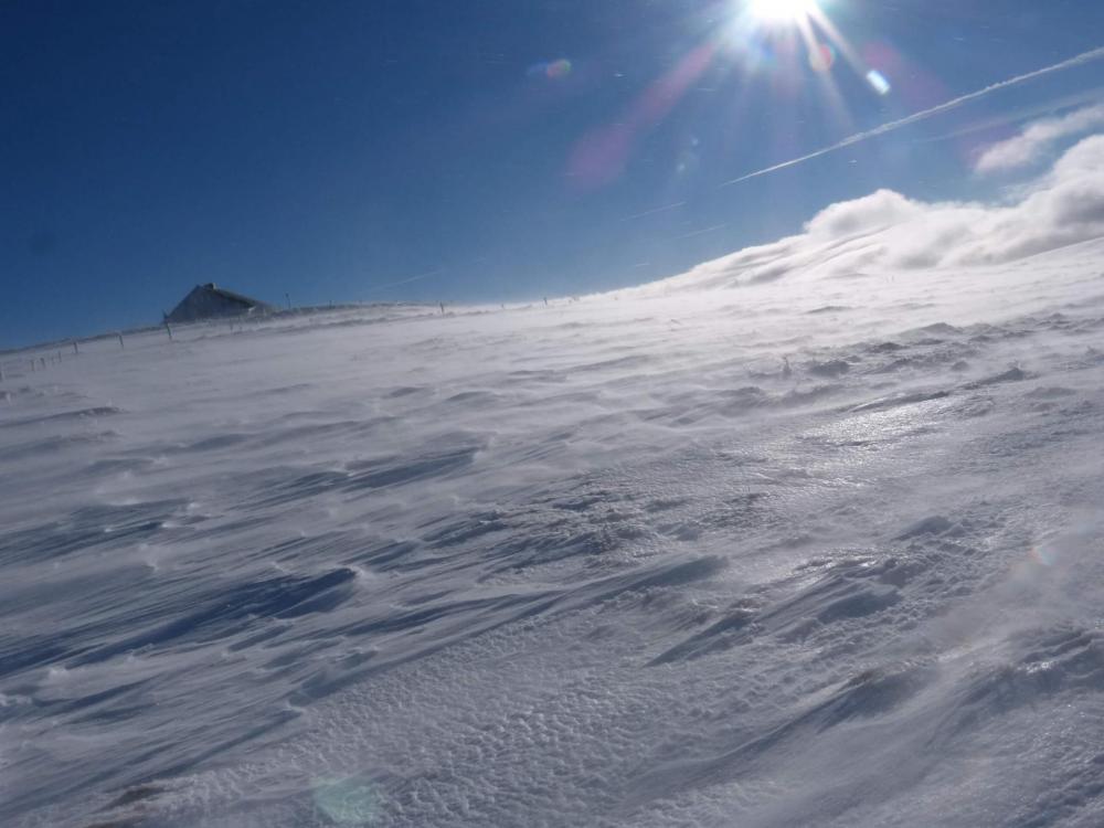 des volutes de neige se soulèvent sous l' effet du vent, et une barre nuageuse s' approche sur la droite